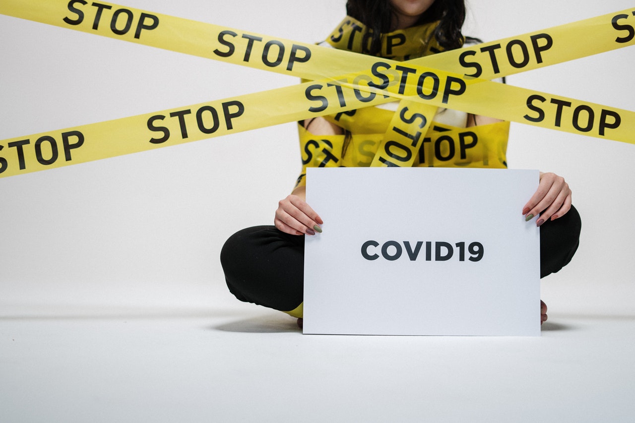 A woman holding a covid-19 sign surrounded by caution tape reading "stop"