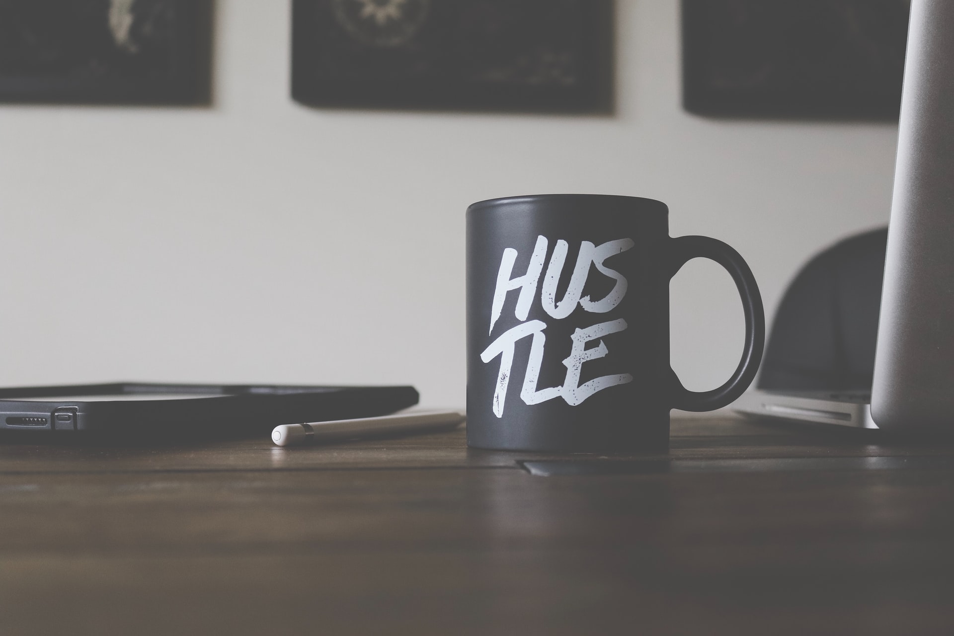 a black coffee mug on an office desk with the word "hustle" on it, representing entrepreneurship